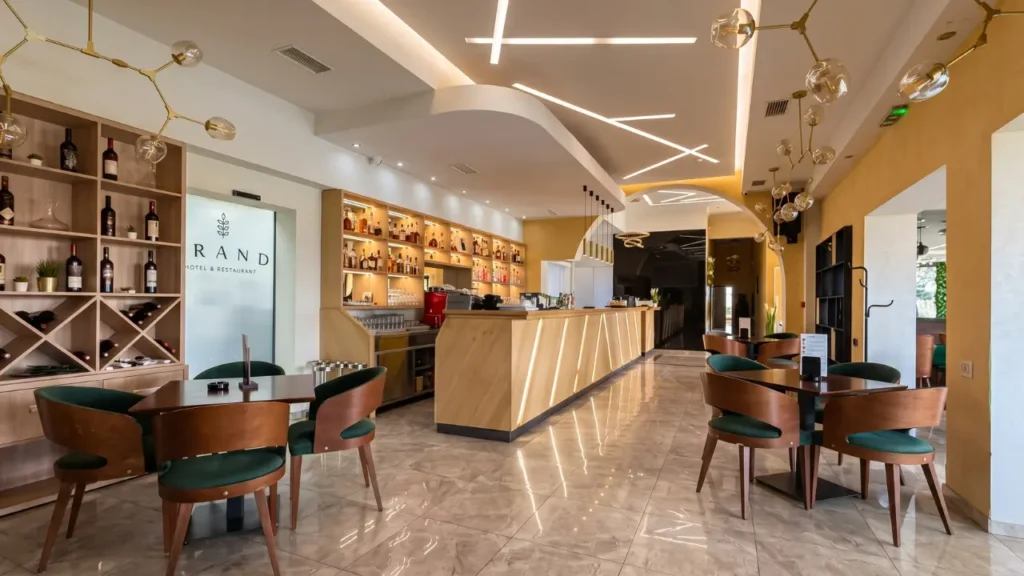 Spacious interior featuring a wooden bar, green armchairs, and modern geometric lighting - Grand Hotel & Restaurant, Backa Palanka.
